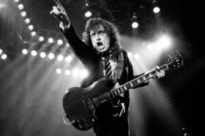 Guitarist of the Band AC/Dc Angus Young holding his guitar and pointing to the crowd while on stage.