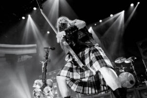 Zach Wylde from the Band Balck label Society on stage rocking out with his guitar and wearing a plaid kilt.