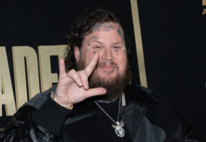 Jelly Roll flashing the Rock N Roll Devil Horns with his left hand posing for a picture