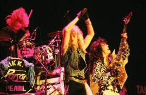 Brett Michaels, lead singer of poison shown clapping his hands in the air  performing with the band on stage in the 80's.
