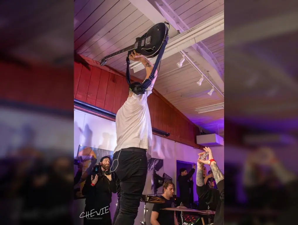 The Dillinger Escape Plan's guitarist Ben Weinman holds his guitar up while standing on top of Billy Rymer's kick drum.